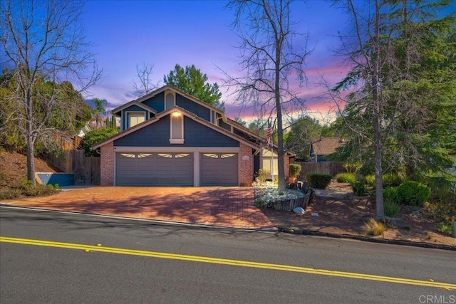 view of front facade with a garage, decorative driveway, brick siding, and fence