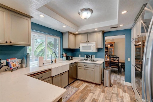 kitchen featuring visible vents, dishwasher, white microwave, a tray ceiling, and light countertops