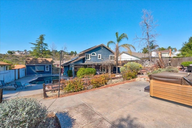 view of front facade with a patio, a fenced backyard, an outdoor structure, an outdoor pool, and a hot tub