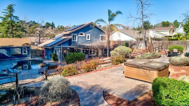 view of front of house with a hot tub, a fenced backyard, an outdoor structure, a patio area, and roof mounted solar panels