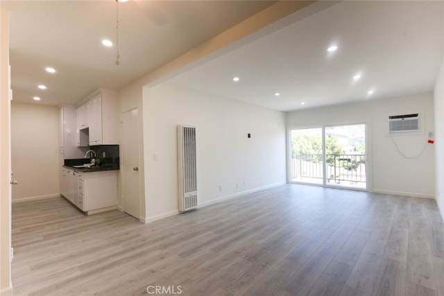 unfurnished living room featuring light wood-style flooring, recessed lighting, a sink, baseboards, and an AC wall unit