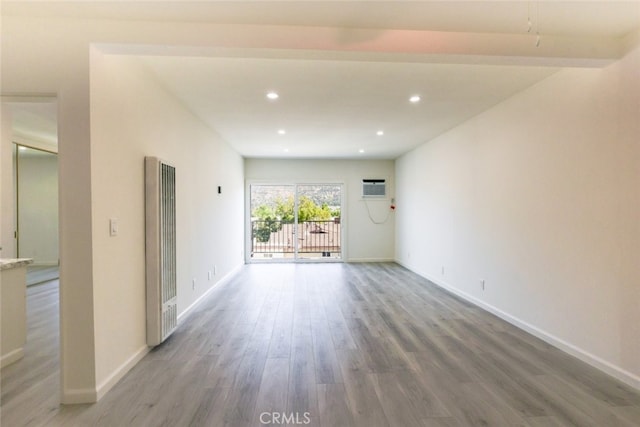 unfurnished room featuring recessed lighting, an AC wall unit, baseboards, and wood finished floors