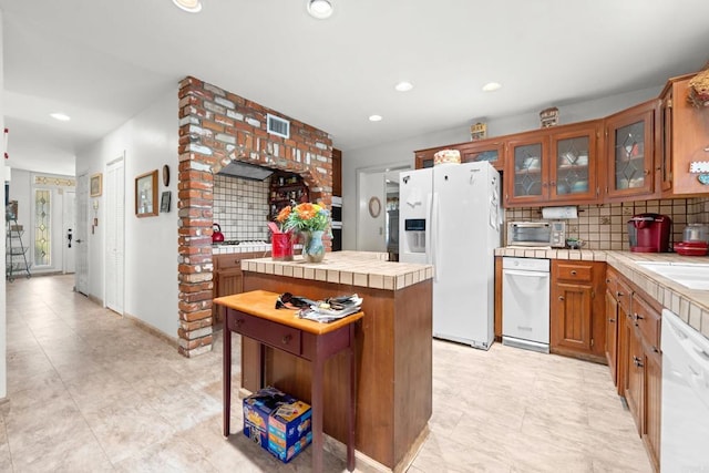 kitchen with white appliances, tile counters, glass insert cabinets, brown cabinets, and backsplash