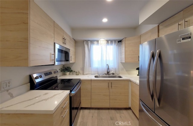 kitchen with a sink, light brown cabinets, light wood finished floors, and stainless steel appliances