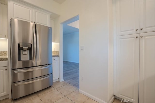 kitchen featuring white cabinetry, baseboards, stainless steel fridge, and light tile patterned floors