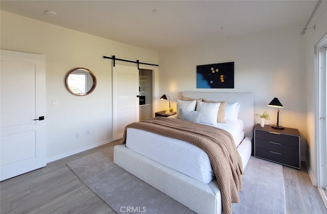 bedroom with baseboards, a barn door, and wood finished floors