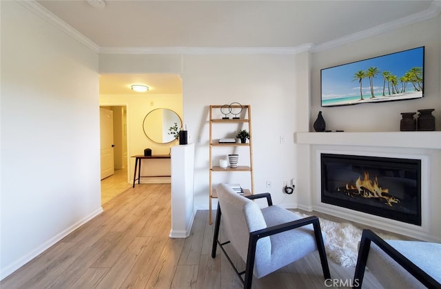living area featuring crown molding, baseboards, a glass covered fireplace, and light wood-style floors
