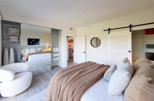 bedroom with visible vents, a barn door, wood finished floors, and a closet