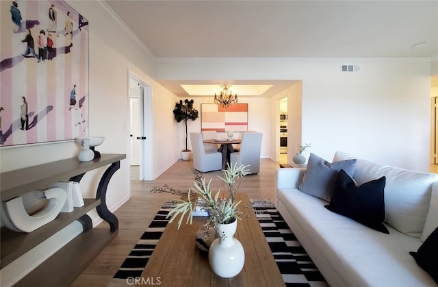 living area with visible vents, wood finished floors, baseboards, a chandelier, and ornamental molding