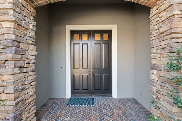 doorway to property featuring stone siding and stucco siding