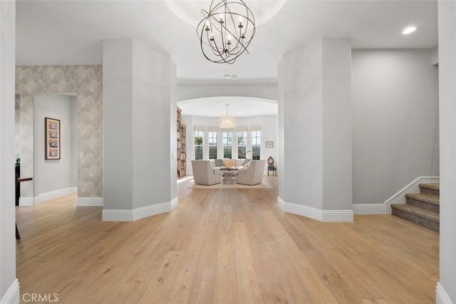 hallway with light wood-style floors, baseboards, and arched walkways