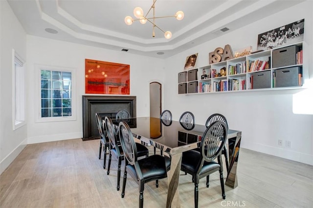 dining space with light wood-style flooring, a fireplace, baseboards, a tray ceiling, and an inviting chandelier