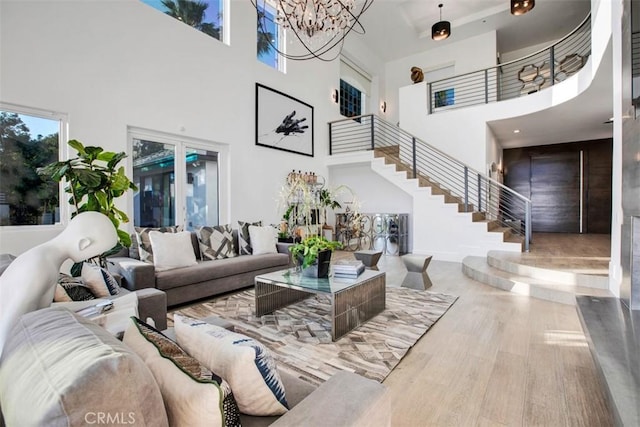 living area with a towering ceiling, wood finished floors, a chandelier, baseboards, and stairs