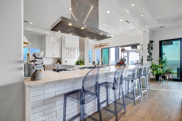 kitchen featuring island exhaust hood, glass insert cabinets, white cabinets, a peninsula, and a kitchen breakfast bar