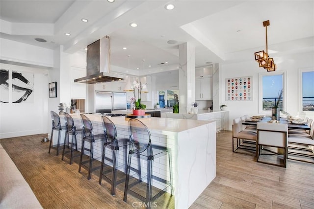 kitchen with light wood finished floors, island range hood, decorative light fixtures, light countertops, and white cabinetry