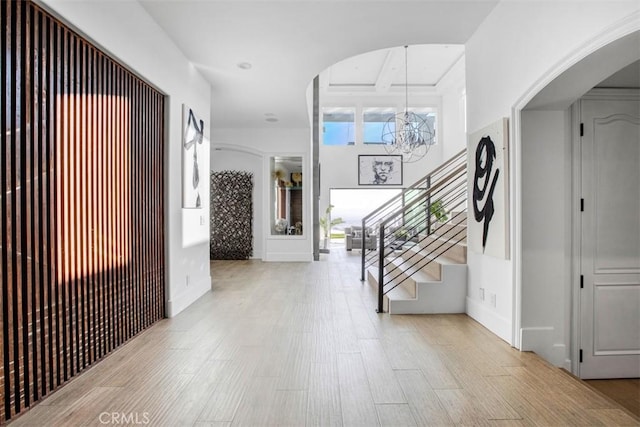 entryway featuring a chandelier, light wood finished floors, stairway, and arched walkways