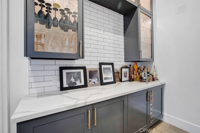 bar featuring light wood finished floors, visible vents, baseboards, a bar, and backsplash