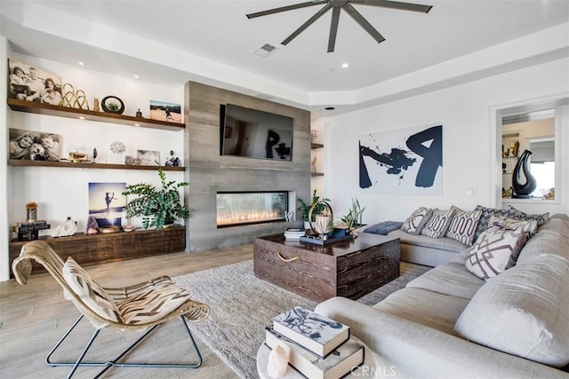 living area with built in features, a fireplace, recessed lighting, ceiling fan, and light wood-type flooring