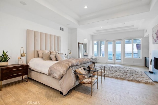 bedroom with french doors, a tray ceiling, a water view, and access to exterior