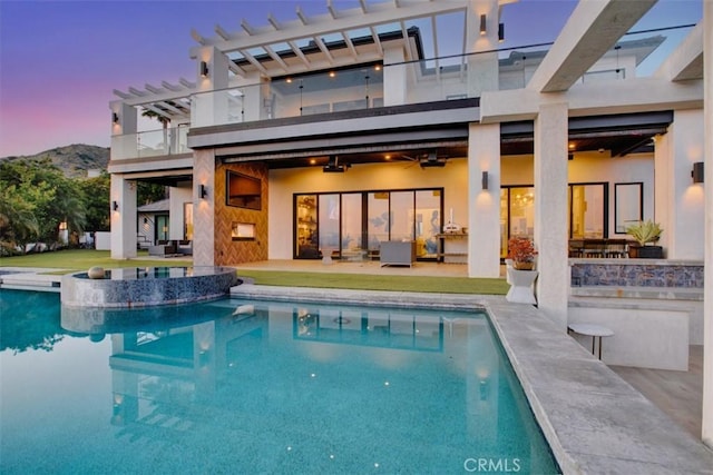 back of property at dusk with a balcony, a patio area, an outdoor pool, and stucco siding