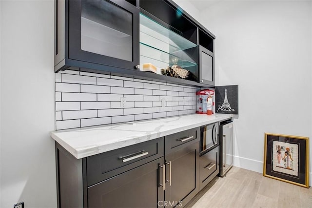 bar with light wood-type flooring, tasteful backsplash, baseboards, and beverage cooler