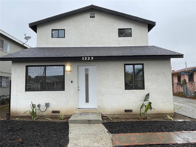 view of front of house with a shingled roof, crawl space, fence, and stucco siding