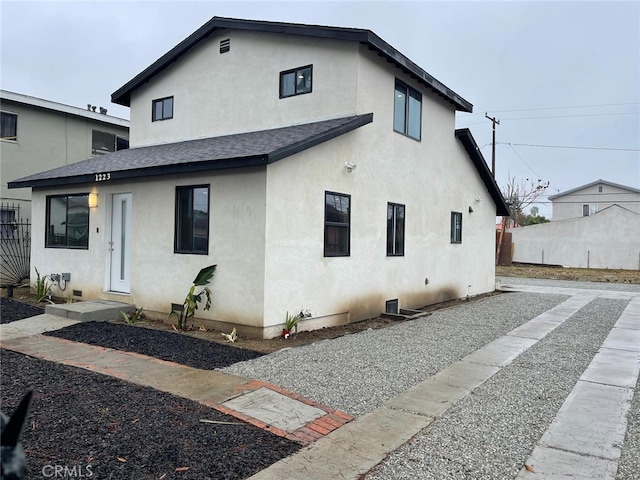 view of front of house with roof with shingles, fence, and stucco siding