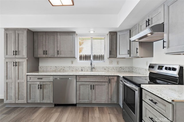 kitchen featuring light stone counters, appliances with stainless steel finishes, dark wood-style flooring, under cabinet range hood, and a sink