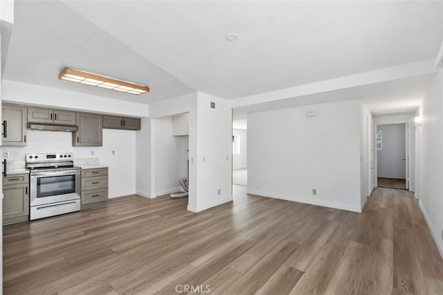 kitchen featuring baseboards, wood finished floors, under cabinet range hood, light countertops, and stainless steel range with electric stovetop