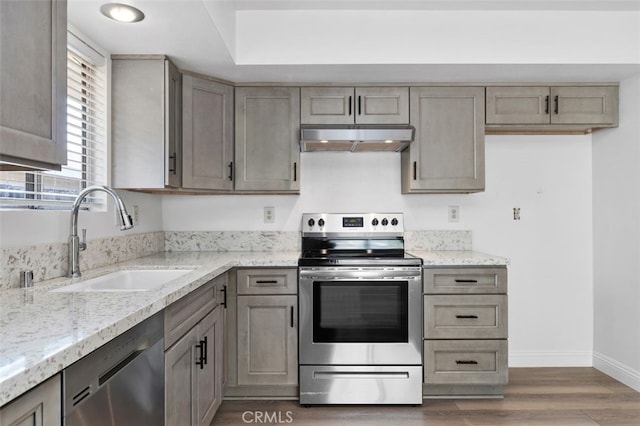 kitchen featuring light stone counters, wood finished floors, stainless steel appliances, under cabinet range hood, and a sink