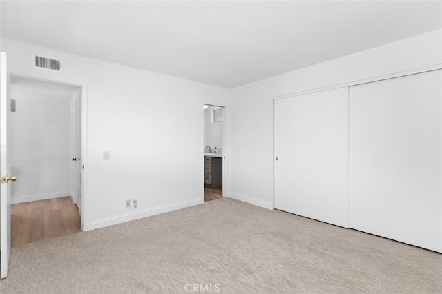 unfurnished bedroom with baseboards, visible vents, connected bathroom, light colored carpet, and a closet