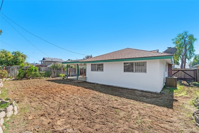 rear view of house with a fenced backyard, central AC, and stucco siding