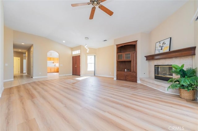 unfurnished living room with baseboards, a ceiling fan, a tile fireplace, vaulted ceiling, and light wood-type flooring