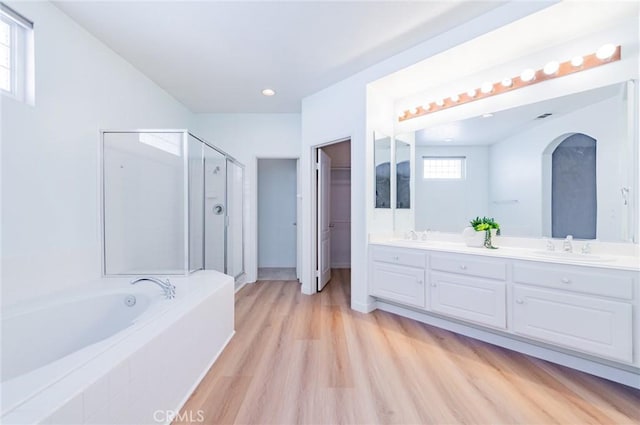 full bathroom with a garden tub, double vanity, a sink, a shower stall, and wood finished floors