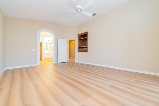 unfurnished room with light wood-type flooring, arched walkways, visible vents, and baseboards