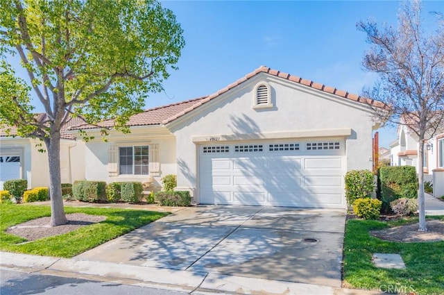 mediterranean / spanish-style home with a tile roof, stucco siding, an attached garage, and concrete driveway