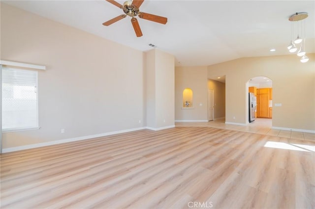 empty room featuring lofted ceiling, ceiling fan, arched walkways, light wood-style flooring, and baseboards