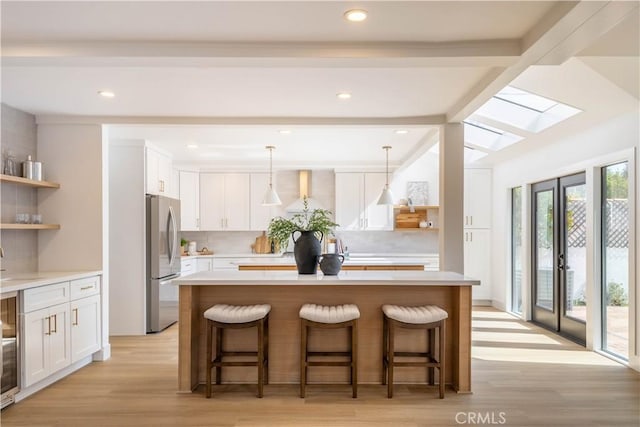 kitchen featuring open shelves, a center island, freestanding refrigerator, a breakfast bar area, and wall chimney exhaust hood