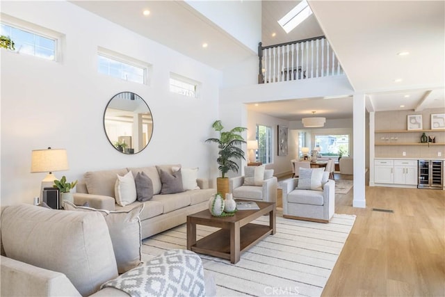 living room featuring recessed lighting, light wood-style floors, beverage cooler, and a towering ceiling