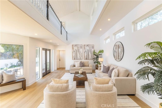 living room with french doors, baseboards, light wood-style floors, and a high ceiling