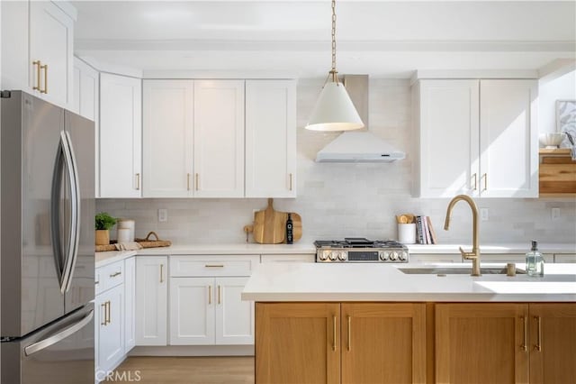 kitchen with a sink, appliances with stainless steel finishes, light countertops, and wall chimney range hood