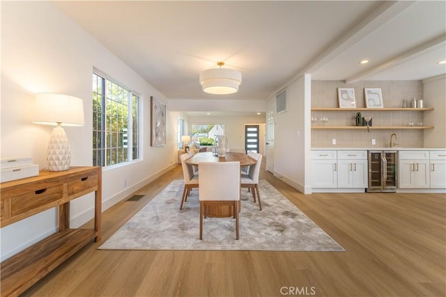 dining area featuring beverage cooler, visible vents, light wood finished floors, baseboards, and wet bar