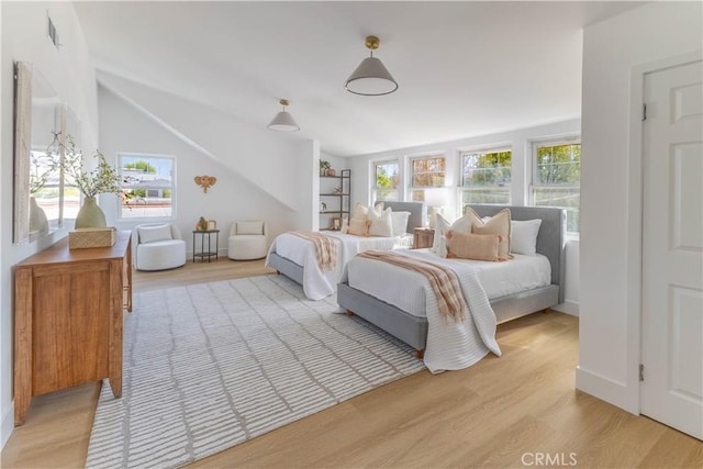 bedroom featuring visible vents, light wood-type flooring, baseboards, and vaulted ceiling