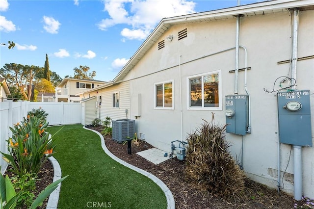 view of side of home with cooling unit, a fenced backyard, a lawn, and stucco siding