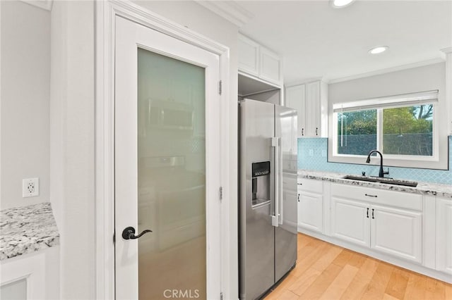 kitchen with light stone counters, white cabinets, stainless steel fridge, and a sink