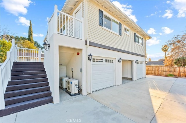 exterior space featuring a balcony, an attached garage, stairs, fence, and ac unit