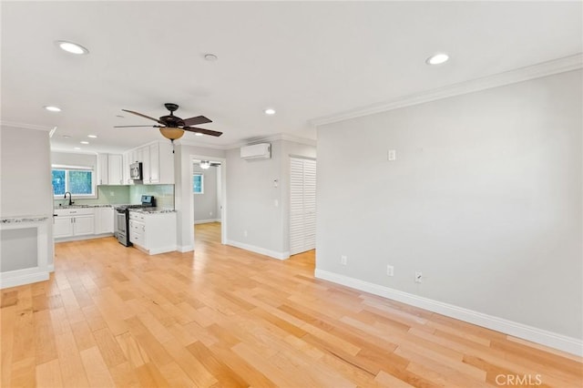 unfurnished living room with baseboards, a wall unit AC, light wood-style flooring, ornamental molding, and a sink