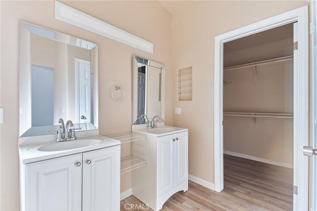 full bathroom featuring two vanities, a sink, baseboards, and wood finished floors