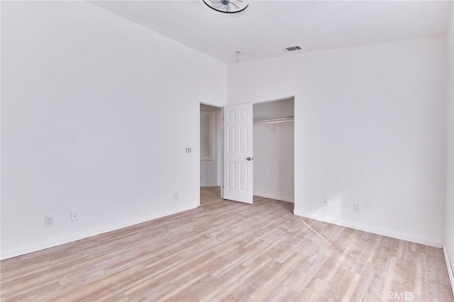 unfurnished bedroom with lofted ceiling, a closet, visible vents, light wood-style floors, and baseboards