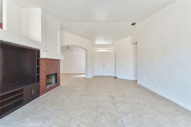 unfurnished living room featuring arched walkways, light tile patterned flooring, visible vents, vaulted ceiling, and a tiled fireplace